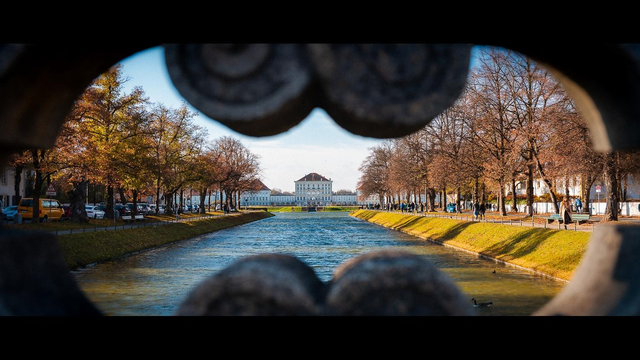 Blick durch eine öffnung in einem steinernen Brückengeländer entlang eines Kanals zu einem breiten Schloss.