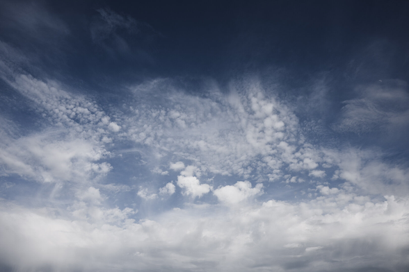 A wide angle photograph of a half cloudy sky with a very complex texture of different types of white clouds.

At the bottom is a heavy layer of clouds along the edge, and along the top the sky is almost clear blue.

In between are a multitude of different cloud shapes, from large fluffy clouds to small ones and longer streaks of thin wispy clouds.

Somewhere in the photograph, the moon can be seen, very small in the frame.
