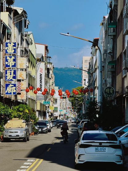 繁忙的街道，两侧高楼上挂满红灯笼，远处有山和蓝天。