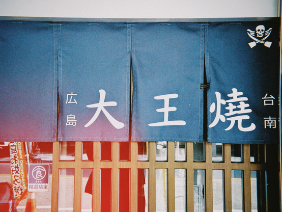 这是一个店铺的门帘，上面有日语文字“大王烧”，旁边写有“广岛” 和“台南”。