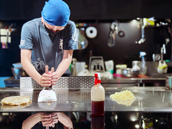 厨师正在厨房里用模具制作面食，桌上有面饼和面条，背景是厨房用具。