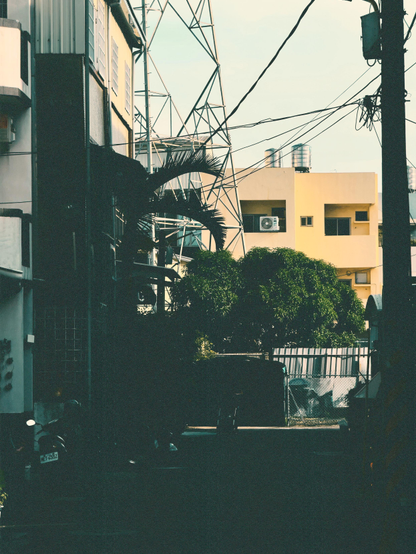 A sunny urban scene with buildings, trees, power lines, and a motorcycle parked on the street.