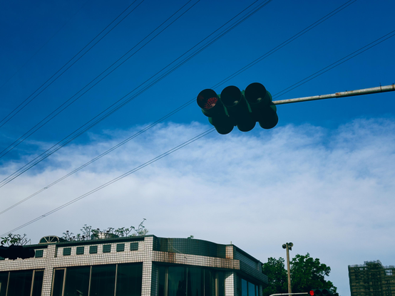 Traffic light with red signal against a blue sky and a building in the background.