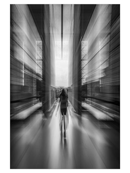 Das Schwarz-Weiß-Bild ist ein ICM-Bild, während der Aufnahme wurde die Brennweite kontinuierlich verkleinert. Das Bild zeigt eine Person, die sich einer großen geöffneten Pforte mit vielen Glaselementen nähert um das Gebäude zu verlassen. Von außerhalb des Gebäudes fällt helles Licht in den Raum