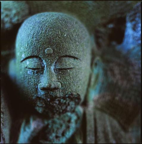 colour photograph of a small buddha, in low light. the colours tend to blue and green. out of focus highlights are almost a neon blue.