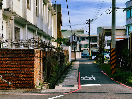 宽敞的街道两旁有建筑物，电线杆上有电线，街道上有车停放，天空晴朗。