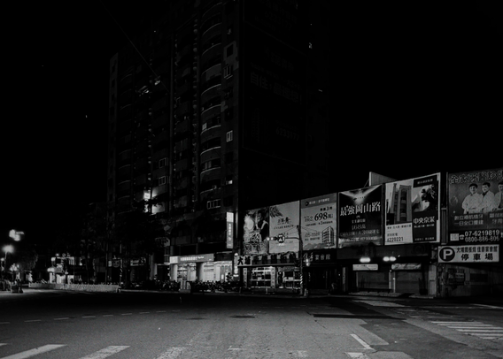Empty city street at night with illuminated billboards and buildings in black and white.