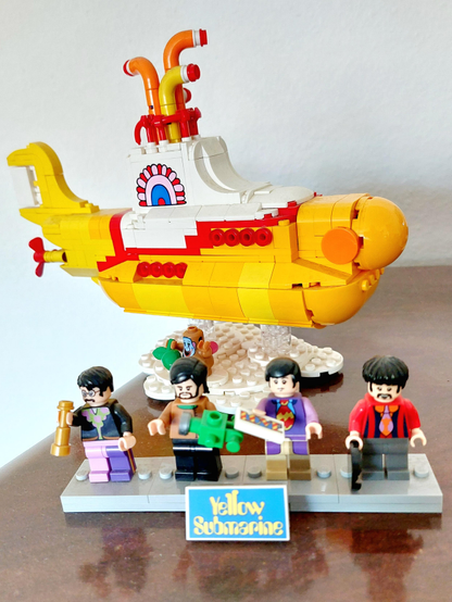 A submarine built from LEGO in a Pop Art style, in yellow, orange and red. In front of it stand four small figures representing the four Beatles: John Lennon, Paul McCartney, George Harrison and Ringo Starr. In front of them is a turquoise sign with the words 'Yellow Submarine' in yellow lettering. 

The original film ‘Yellow Submarine’ is an animated film directed by George Dunning, released in 1968. The film’s soundtrack was composed by the British band The Beatles and George Martin, and was released in 1969 on the album ‘Yellow Submarine’.