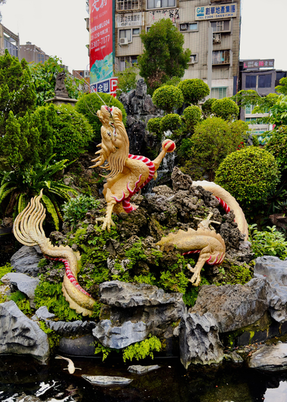 花园中的一只金色龙雕塑，背景是繁华的城市建筑和绿意盎然的植物。