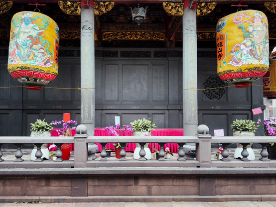祭祀场所，两盏彩色灯笼悬挂，古建筑背景，有花卉盆栽和祭祀用品。