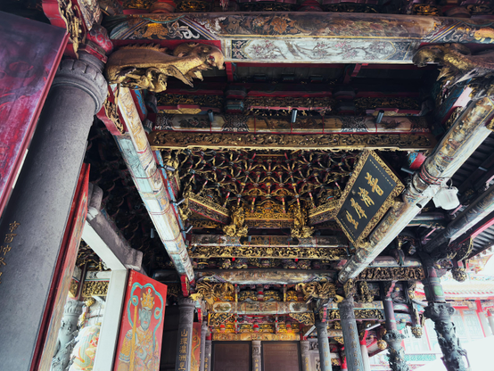 这是一个精美的中式建筑天花板，装饰有金色雕刻和传统图案，柱子上有狮子和龙的雕塑。