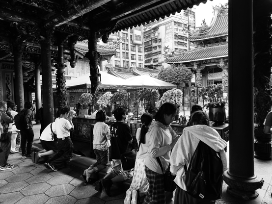 在寺庙前祈祷的多位信徒，背景有建筑和祭祀用品，场景充满祈福氛围。