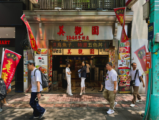 这是一家名为“美観園”的日式餐厅，成立于1946年，门前有几个人在走动和交谈。