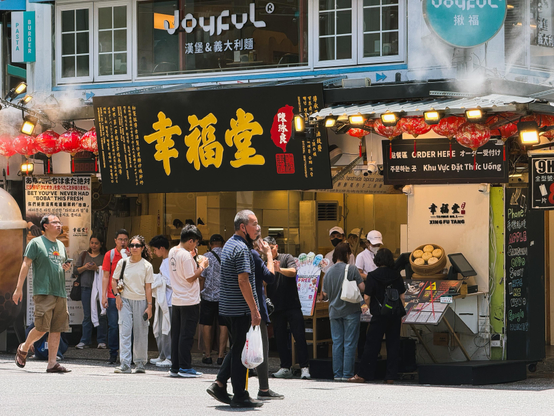 街头排队买点心的人群，店面招牌写有“幸福堂”，有红灯笼和多语言菜单。