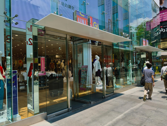 一间百货商店的玻璃门外，有几个人正在走过，商店内部展示各种衣物，墙上有多块彩色广告牌。