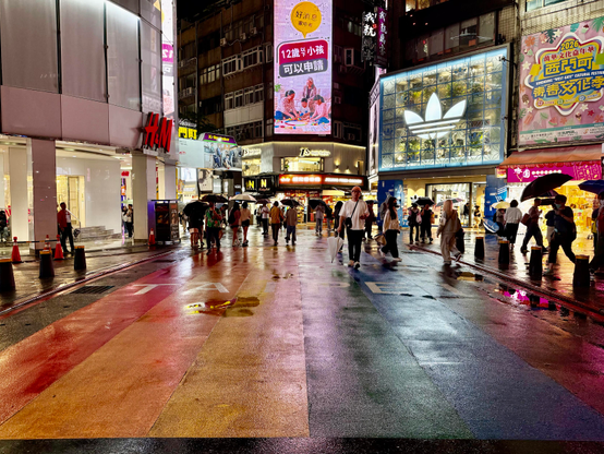 雨中繁华街道，行人撑伞走过，街道湿润反光，霓虹广告灯火辉煌。