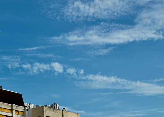 Clear blue sky with scattered white clouds over the rooftops of buildings.