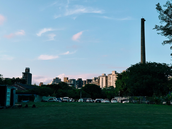 City skyline with modern buildings and a tall chimney, taken during the day with a bright blue sky and some clouds.