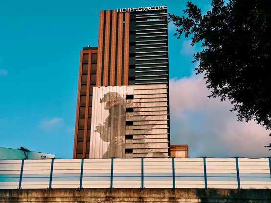 The tall building labeled "Hotel Gracery" has a large dragon mural on its side, with a clear blue sky in the background.