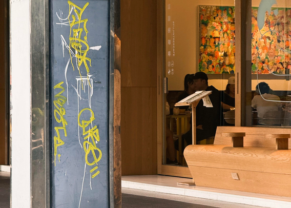People dining inside a restaurant, visible through a glass door, with colorful artwork on the wall behind them.