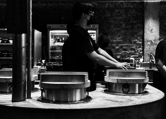 People wearing masks preparing food behind a counter in a restaurant.