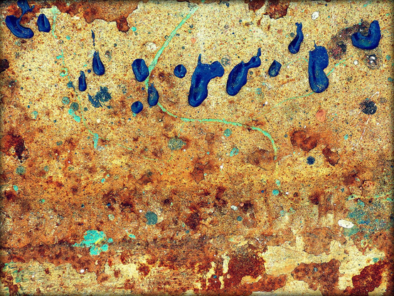 A colour abstract photograph showing drips of blue paint on old steel plate with rust emerging through cream-coloured paint. A thin winding snake of green paint passes vertically through the drips towards the top of the frame.