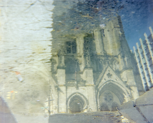 The Gothic Cathedral of St. John the Divine reflected in a puddle on wet pavement after rain