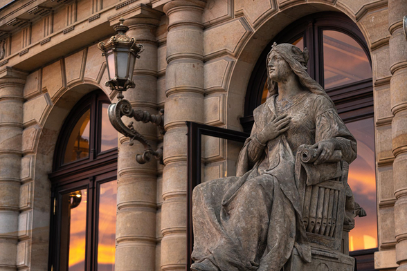 photo of a statue of a muse waiting in front of the Rudolfinum in Prague. the photo was taken at sunset. dramatic clouds are reflected in teh windows behind the statue. 