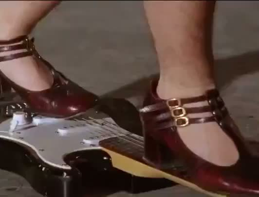 une jeune musicienne punk joue de la guitare en la piétinant, puis la brise
