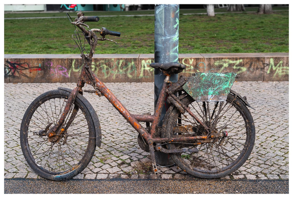 Ein von Arbeitern aus der Spree geangeltes, vollig verdrecktes Fahrrad lehnt an einem Laternenpfahl.