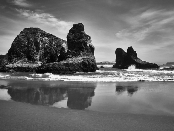 rock formations on a beach as the tide flows in and out. Their reflections bounce off the wet sand and high clouds float way above
