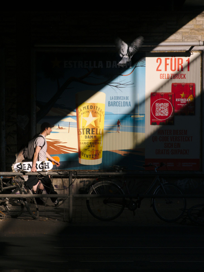 Diagonal light, a beer advert, a person walking through the scene, a pigeon overhead.