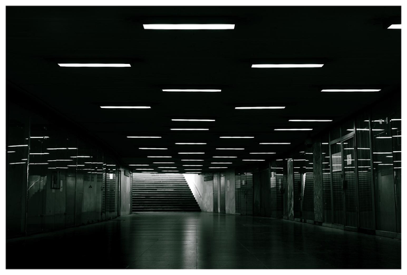 Menschenleere Unterführung in Schwarz/Weiß. Am Ende eine Treppe von deren oberen Ende Licht ins Dunkel fließt.