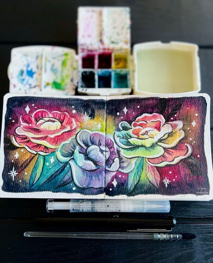 My watercolor and ink painting of a glowy bouquet of 3 peonies in a row in my sketchbook. Also in the photo are my paint palette, watercolor paint, and paint brush, and ink brushes.