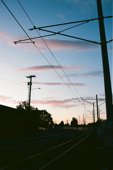 A deep blue sky with pink clouds over silhouetted light rail lines and power poles.