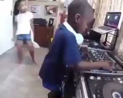 deux enfants noirs dans un salon de musique, le garçon à la table de mixage, la fille danse