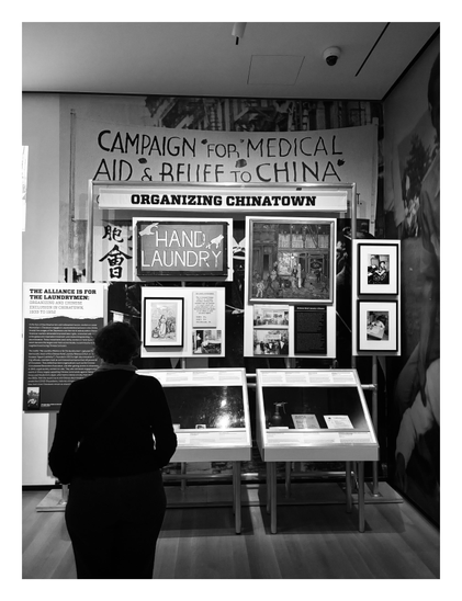 Black and white photo of a display of documents, photographs, signs, and other items at a museum exhibition. Prominent signs and placards read “Organizing Chinatown,” “HAND LAUNDRY,” “Campaign for Medical Aid & Relief to China,” and “The Alliance is for the Laundrymen: Organizing and Chinese Exclusion in Chinatown, 1933-1952.” A person with their back to the camera stands looking at the display.

This is part of the longstanding exhibition “Activist New York” in the Museum of the City of New York, which will soon close to make way for the museum’s new permanent Puffin Foundation Center for Social Activism.