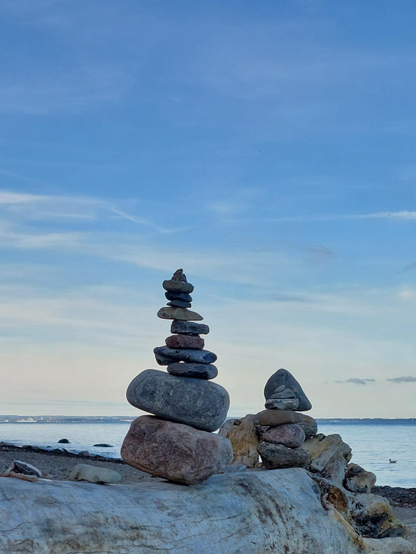 Two cairns, made of round, stacked stones, stand on the shore, gazing into the distance, contemplating the endless blue of the sea and the sky and pondering the insignificance of humanity itself.