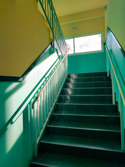 Fotografía de una escena, unas escaleras suben, la forma que incide la luz que entra a traves de una ventana en la parte superior , los colores y la composición completan la imagen.