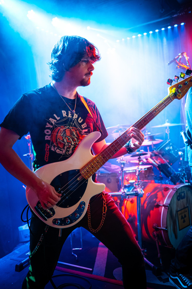 Das Foto zeigt Felix, den Bassisten der Band Lunar Fall, der mit seinem E-Bass in den Händen auf der Bühne vor dem Schlagzeug steht.
