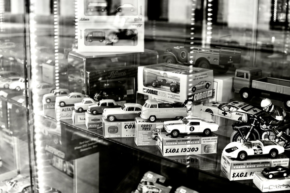 Picture shows a detailed shot of toy cars in a shop window. Cars are presented on tiny boxes and are older models. 