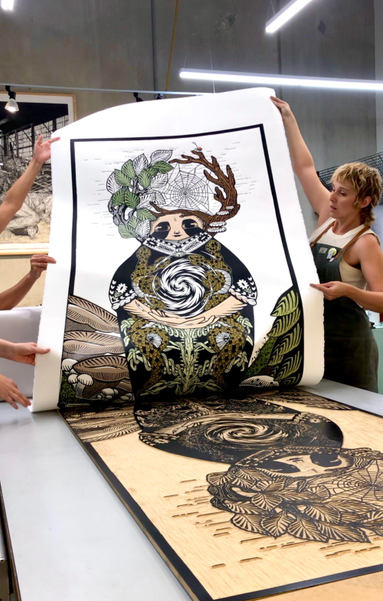 a large woodblock print being pulled by two artists