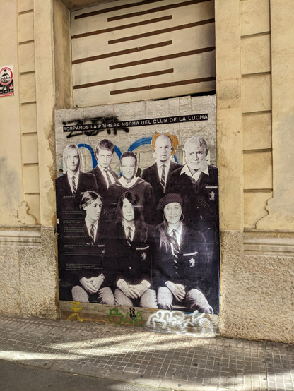 A picture of a house wall with a big poster, showing eight humans. All are dressed in school uniforms. Persons are famous/prominent and all died by suicide. 