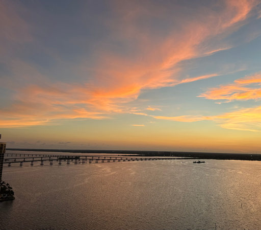 Blue river with pink reflections from the pink and yellow clouds above. Sky is blue and the horizon has an ombre haze. 