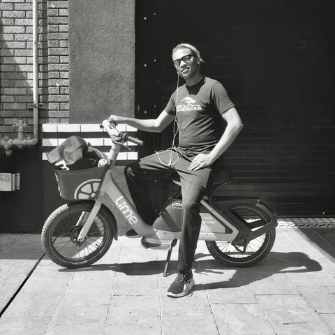 A black-and-white film photo. Nigel, who is seated on an electric scooter, is headed off to work in downtown Austin, Texas. Saturday, June 6, 2026.
