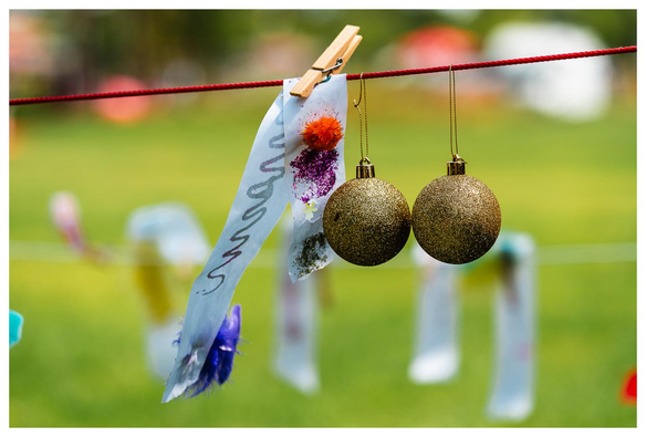 Goldene Weihnachtsbaumkugeln und ein länglicher Zettel hängen an einer Wäscheleine in einem Park.