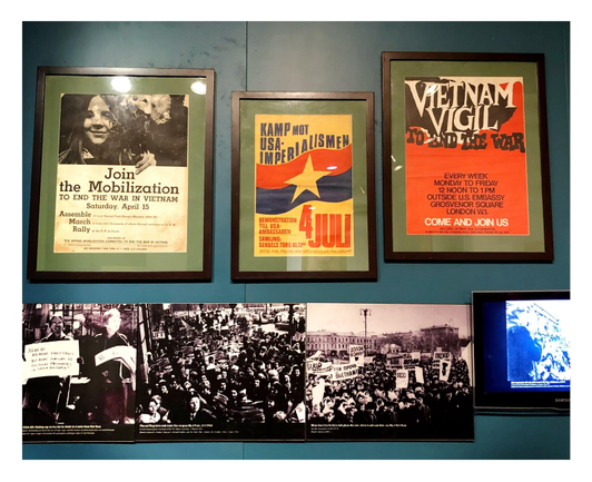 A wall display of three framed posters announcing marches and vigils against the Vietnam War, taking place in New York, Stockholm, and London. Underneath is a row of monochrome photographs showing heavy attendance at these international protests.
