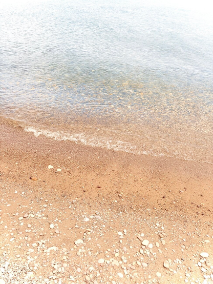 Photograph of a golden brown sand beach, with small pebbles at the bottom of the photo and clear water with a turquoise tint at the top, reflecting the light. A small ripple crashing on the sand creates a diagonal line about the middle of the photo. A little editing has been done, to remove contrast and add light, to give a soft and dreamy appearance to the photo.

Photographie d'une plage de sable brun doré, avec de petits galets dans le bas de la photo et l'eau claire avec une teinte turquoise dans le haut, reflétant la lumière. Une petite vaguelette s'écrasant sur le sable crée une ligne diagonale à peu près au milieu de la photo. Un peu d'édition a été fait, pour enlever du contraste et ajouter de la lumière, pour donner une apparence douce et de rêve à la photo.