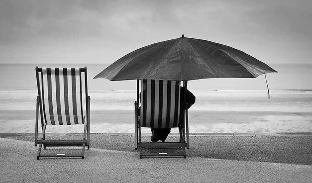 à la limite de l'eau, protégé du ciel par un énorme parasol, un homme dans un transat au centre d'un espace délimité par le sable, la mer et le soleil