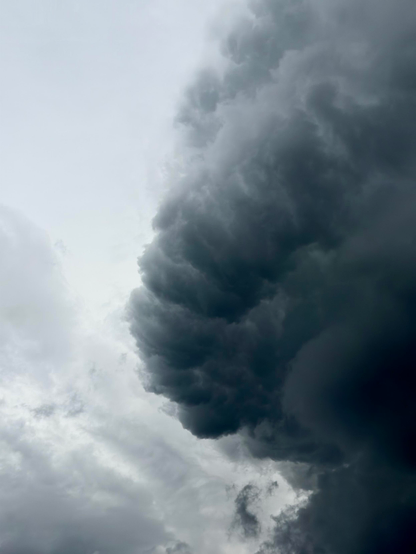 Ein dramatischer Blick auf dunkle, wirbelnde Gewitterwolken vor einem helleren Himmel, der eine stimmungsvolle und atmosphärische Szene schafft.